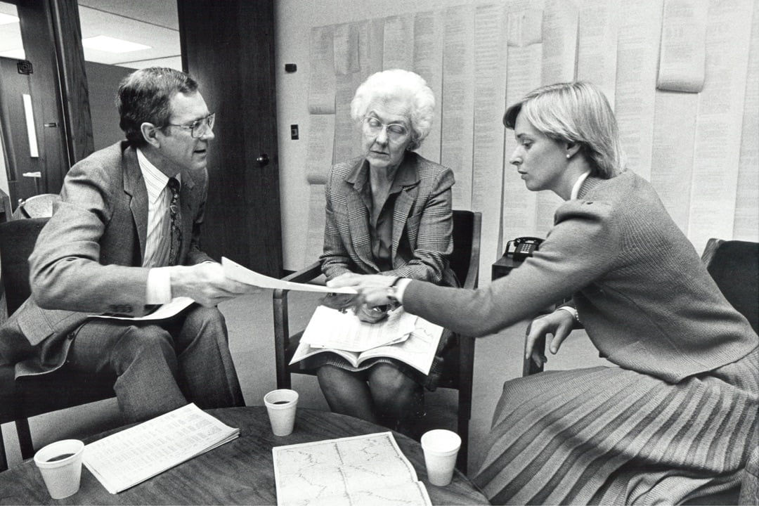 Photo from 1984 of Capital Group associates sitting around a small table discussing a report.
