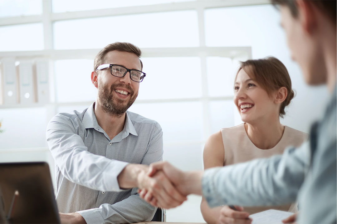 Two men shaking hands while a woman looks on smiling. 