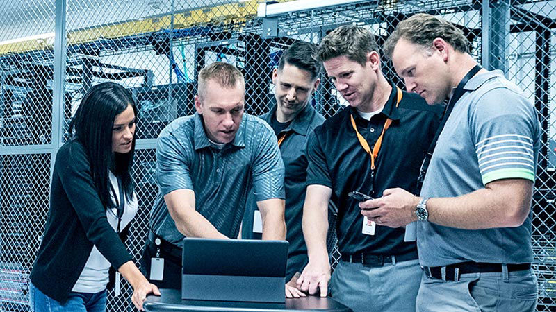 Five workers, four men and one woman, looking at at a computer screen. 